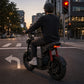 Person riding an electric scooter at a city intersection with traffic lights and buildings in the background. - windhorse d1
